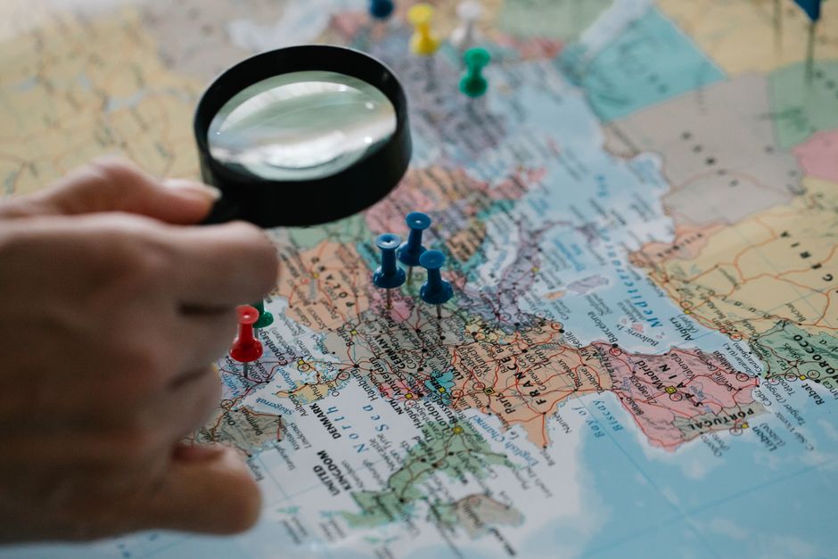 Magnifying glass focuses on pins highlighting travel destinations on a world map.